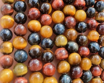 May include: Close-up of a collection of polished, round tiger eye gemstone beads. The beads display a range of colors, including golden brown, deep red, black, and blue. The beads are strung together, showcasing their natural patterns.