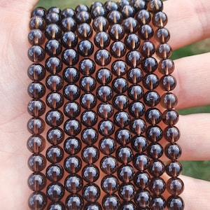 Peut inclure: Un brin de perles de pierres précieuses brun foncé, probablement du quartz fumé, avec une légère brillance dorée. Les perles sont rondes et de taille uniforme, enfilées sur un cordon fin.