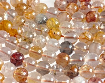 May include: Close-up of a collection of round gemstone beads in various colors, including clear, amber, brown, and burgundy. The beads are strung together on a red string, creating a textured and colorful display. Ideal for jewelry making.