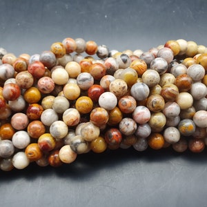 Peut inclure: Un ensemble de perles rondes et polies dans diverses teintes terreuses. Les perles présentent un mélange de beige, de gris, d'orange et de marron, avec des motifs et des textures uniques. Ces perles sont probablement utilisées pour la fabrication de bijoux ou l'artisanat.