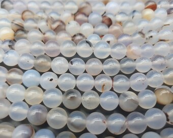 May include: A close-up of a strand of white agate beads. The beads are round and smooth, with a translucent white color and subtle brown and gray markings.