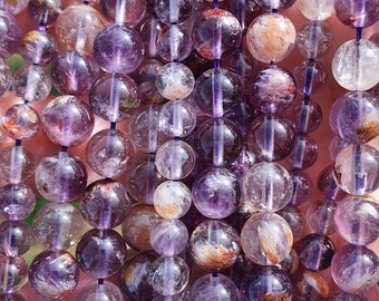 May include: Strands of amethyst beads in varying shades of purple and clear. The beads are round and strung together, showcasing natural inclusions and textures. The beads are approximately 0.5 inches in diameter.