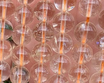 May include: A strand of clear quartz beads with orange inclusions. The beads are round and smooth, and they are strung on a clear elastic cord.