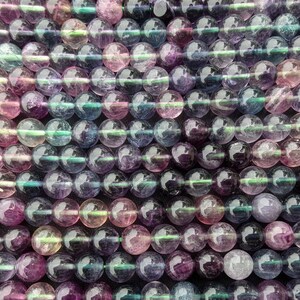 May include: A strand of iridescent rainbow fluorite beads. The beads are round and have a smooth, polished finish. The colours are a mix of purple, pink, blue, and green.