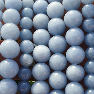 May include: A collection of light blue, spherical beads. The beads vary slightly in size and shade, creating a textured appearance. The beads are strung together, suggesting they are for jewelry making or crafts.