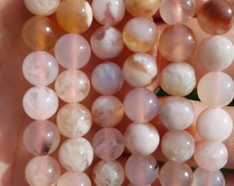 May include: A strand of white agate beads with brown and orange inclusions. The beads are round and smooth, and they are strung on a clear elastic cord.