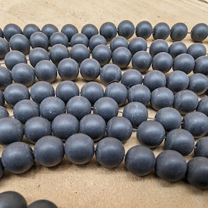 Peut inclure: Un brin de perles noires mates, disposées en quinconce. Les perles sont rondes et lisses, avec une surface légèrement texturée.