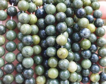 May include: A collection of green jade beads, varying in shades from light to dark, strung together. The beads are round and smooth, with natural variations in color and texture. The beads are displayed against a blurred background.