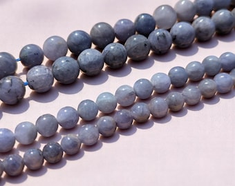 May include: A strand of light blue gemstone beads. The beads are round and smooth, and they are strung on a clear thread. The beads are arranged in a loose, flowing pattern.