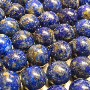 Peut inclure: Gros plan sur plusieurs sphères de lapis-lazuli. Les sphères sont d'un bleu profond avec des inclusions dorées, créant un effet marbré. Les sphères sont lisses et sphériques, réfléchissant la lumière.