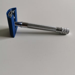 May include: A silver safety razor with a blue plastic handle. The razor has a textured grip and a safety bar.