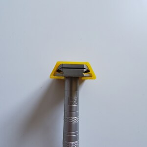 May include: A silver razor with a yellow plastic handle and the letters "HS" engraved on the handle.