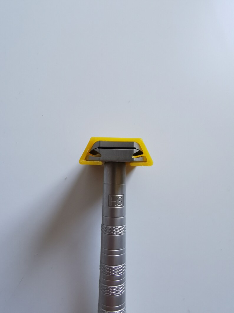 May include: A silver razor with a yellow plastic handle and the letters "HS" engraved on the handle.