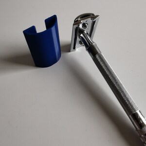 May include: A silver safety razor with a blue plastic stand. The razor has a textured handle and a chrome head.
