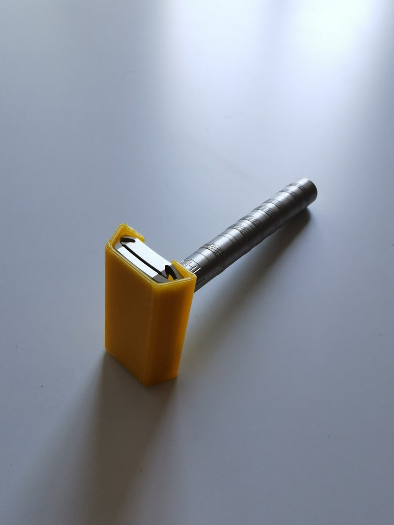 May include: A yellow plastic safety razor with a silver metal handle. The razor is designed to be used with disposable razor blades.