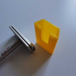 May include: A silver safety razor with a black handle and a yellow plastic stand. The stand has a slot for the razor to fit into.