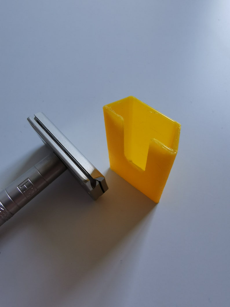 May include: A silver safety razor with a black handle and a yellow plastic stand. The stand has a slot for the razor to fit into.