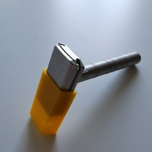 May include: A silver safety razor with a yellow plastic handle. The razor is designed for shaving.