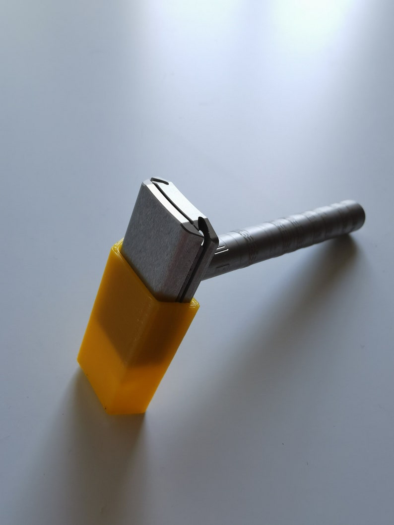 May include: A silver safety razor with a yellow plastic handle. The razor is designed for shaving.