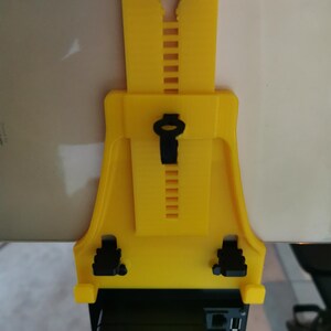 May include: A yellow 3D printed phone holder with adjustable height and a black phone clip. The holder is attached to a black device with multiple ports.