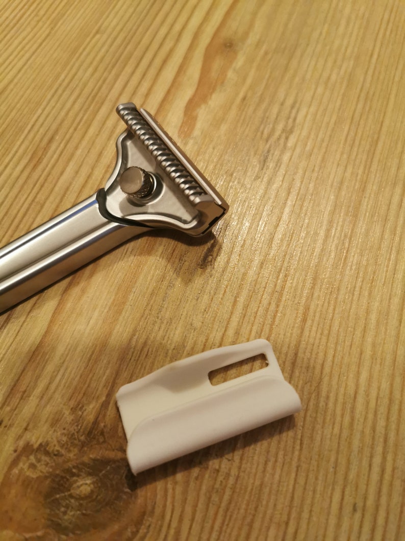 May include: A silver scraper tool with a textured blade and a white plastic handle. The tool is designed for removing wallpaper or other materials.
