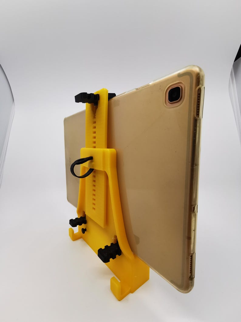 May include: A yellow 3D printed tablet stand with a black adjustable clamp. The stand is designed to hold a tablet in a vertical position.