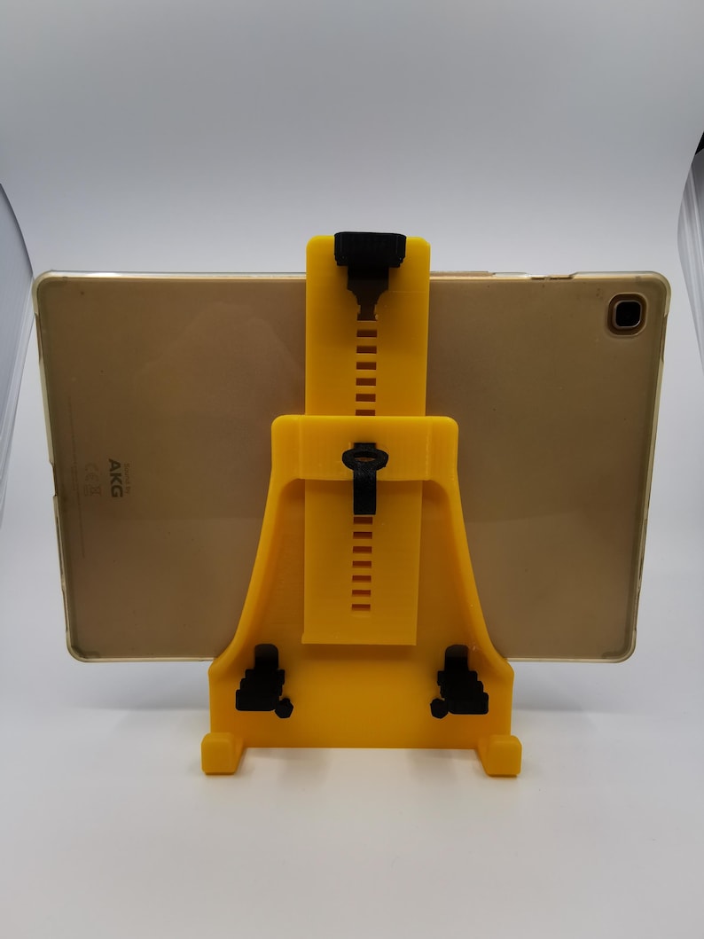 May include: A yellow plastic tablet stand with black adjustable arms. The stand is holding a gold tablet with the text "AKG" on the back.