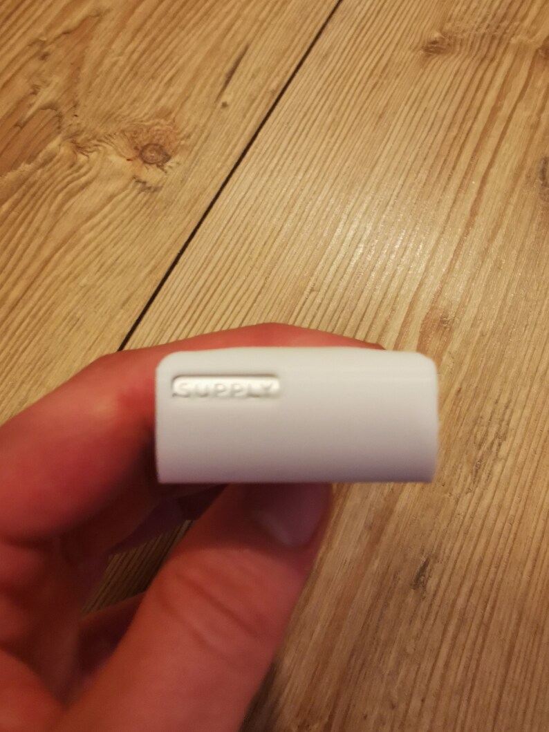 May include: White rectangular power adapter with the word "SUPPLY" printed on it.