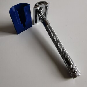 May include: A silver safety razor with a textured handle and a blue plastic stand. The razor has a chrome finish and a classic design.