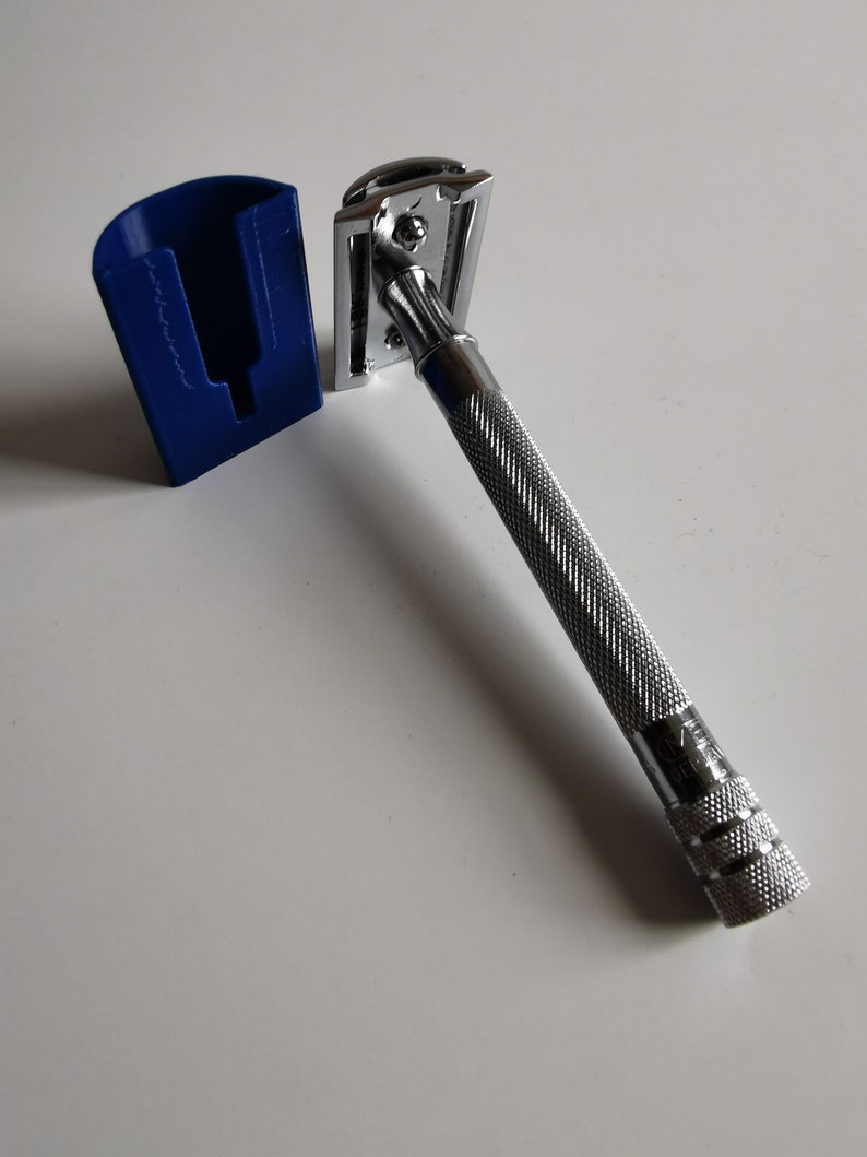 May include: A silver safety razor with a textured handle and a blue plastic stand. The razor has a chrome finish and a classic design.