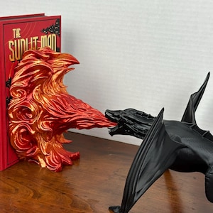 May include: A black dragon bookend with wings spread wide, breathing fire at a red and orange fire bookend. The fire bookend is holding a book titled "The Subtle Man".