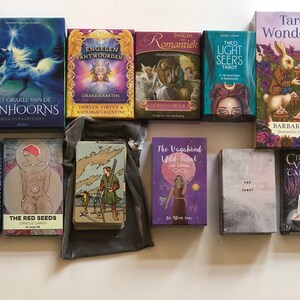 May include: A collection of tarot and oracle decks, including "The Red Seeds Oracle", "Sacred Destiny Oracle", "Crystal Visions Tarot", "The Vagabond Wild Tarot", "The Light Seers Tarot", "Tarot Wonderland", "Life Purpose Oracle", and "Sacred Rebels Oracle".