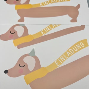 Puede incluir: Tres perros salchicha ilustrados con bufandas amarillas con la palabra "Einladung" escrita en las bufandas. Los perros son marrones con detalles blancos.
