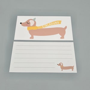 Puede incluir: Una tarjeta blanca en blanco con un dachshund que lleva una bufanda amarilla y un gorro de fiesta. La tarjeta dice "Einladung", que en alem&aacute;n significa "Invitaci&oacute;n".