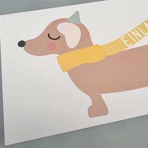 Puede incluir: Un dachshund marr&oacute;n con una bufanda amarilla y un gorro de fiesta con la palabra "EINLAD" en la bufanda.