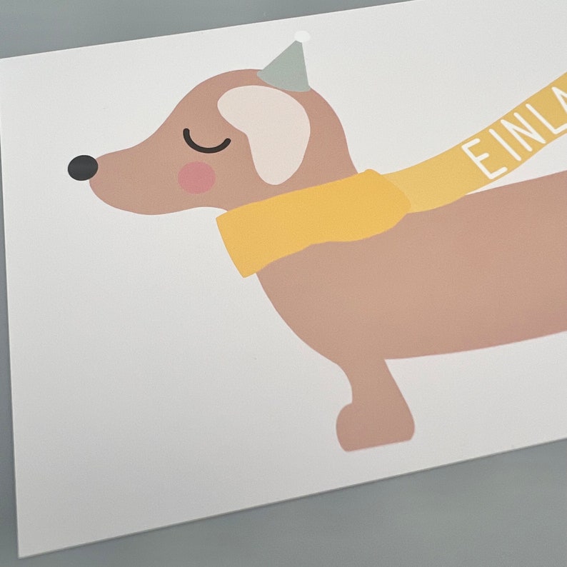 Puede incluir: Un dachshund marr&oacute;n con una bufanda amarilla y un gorro de fiesta con la palabra "EINLAD" en la bufanda.
