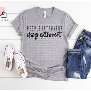 May include: A gray t-shirt with the text "PEOPLE INTROVERT dog extrovert" in black with a paw print replacing the "o" in "dog".