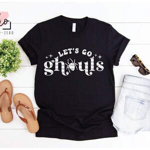 May include: Black t-shirt with a white graphic that says "Let's Go Ghouls" with a spider in the middle of the word "ghouls".