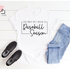 Puede incluir: Camiseta blanca con texto negro que dice "The only BS I need is Baseball Season". La camiseta está colocada sobre una superficie de madera blanca con un par de zapatos negros de vestir y unos vaqueros azules.