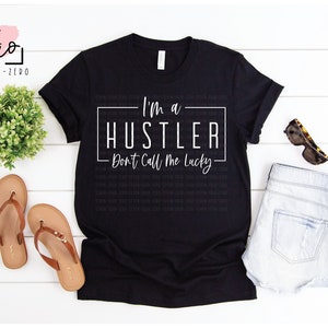 May include: A black t-shirt with white text that reads "I'm a Hustler - Don't Call Me Lucky".
