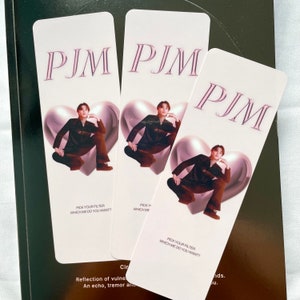 May include: Three pink and white bookmarks with a photo of a person in a black outfit sitting on a large silver heart. The text "PJM" is at the top of each bookmark. The text "Pick your filter, which me do you want?" is at the bottom of each bookmark.