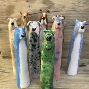 May include: A group of colourful ceramic dog sculptures. The dogs are in shades of blue, green, pink, and tan, with unique patterns and expressions. Some have spots or stripes. They are displayed on a wooden surface.