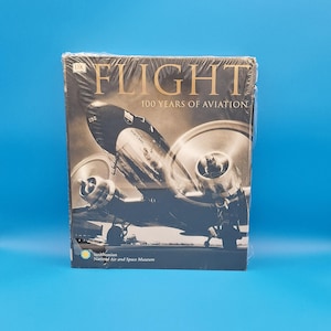 May include: A book titled "Flight 100 Years of Aviation" with a sepia-toned image of a vintage airplane on the cover. The book is sealed in clear plastic and features the Smithsonian National Air and Space Museum logo.