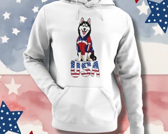 Könnte beinhalten: Ein weißer Kapuzenpullover mit einer Grafik eines Huskys, der eine rot-weiß-blaue Jacke trägt. Unter dem Hund ist der Text USA in einem rot-weiß-blauen Sternenmuster aufgedruckt. Der Hoodie verfügt über eine aufgesetzte Kängurutasche vorne.