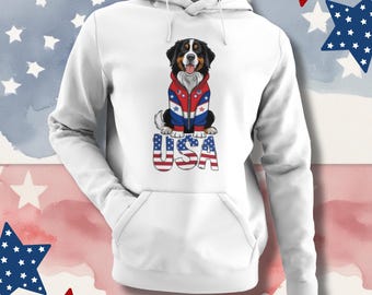 Könnte beinhalten: Weißer Kapuzenpullover mit einer Grafik eines Berner Sennenhundes, der eine rot-weiß-blaue Jacke trägt. Das Wort "USA" ist in einer patriotischen Schriftart unter dem Hund aufgedruckt. Der Hintergrund hat einen Aquarell-Effekt mit Sternen.