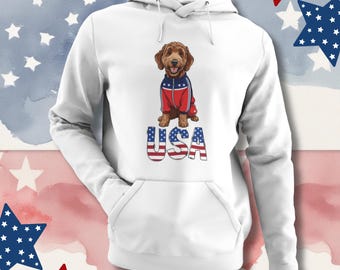 Könnte beinhalten: Weißer Kapuzenpullover mit einem braunen Hund, der eine rot-weiß-blaue Jacke trägt. Das Wort "USA" ist unter dem Hund in einer patriotischen Schriftart aufgedruckt. Der Kapuzenpullover hat eine Vordertasche und eine Kapuze mit Kordelzug.
