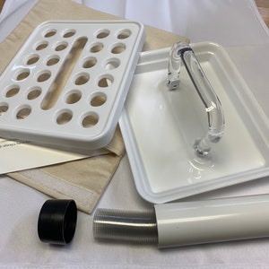 May include: White plastic tray with 24 round holes, a white plastic tray with a clear plastic handle, a black plastic ring, a white plastic tube, and a clear plastic tube with a ribbed texture.