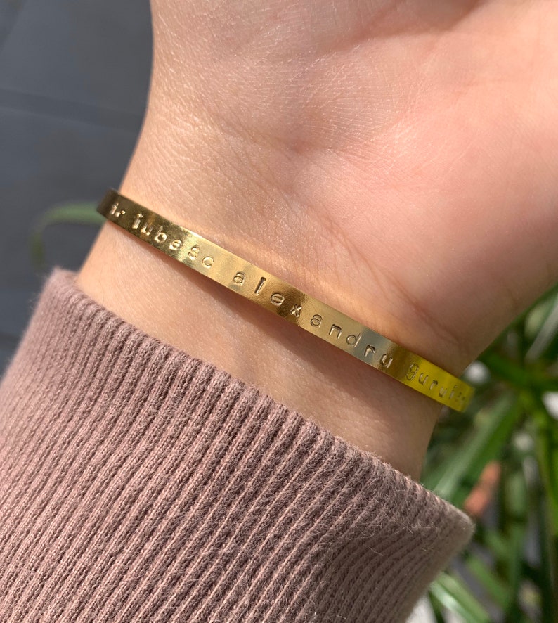 May include: A gold-toned bangle bracelet with the inscription "hubsc alexandru gucci" engraved on the band.