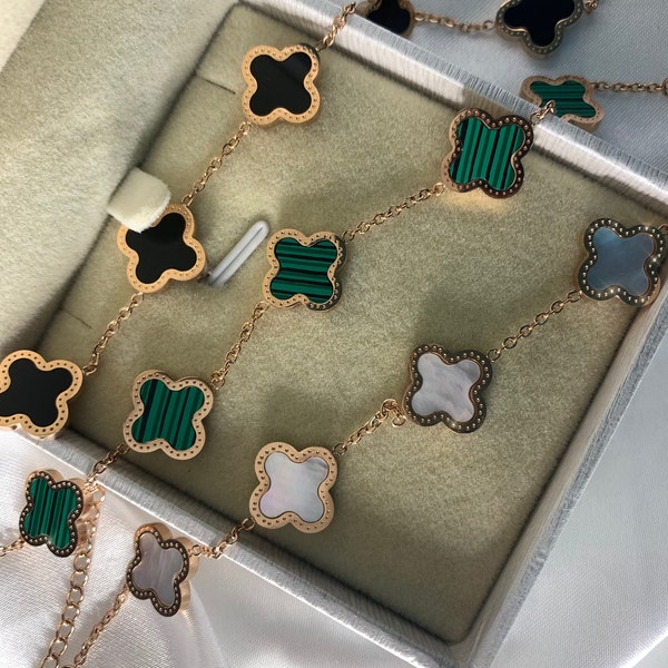 May include: Two gold necklaces with four-leaf clover charms. The charms are made of black, green, and white materials.