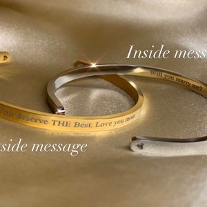 May include: Two gold bangle bracelets with engraved messages. The outside bracelet reads "You deserve THE Best. Love you most." The inside bracelet reads "Will you marry me?"